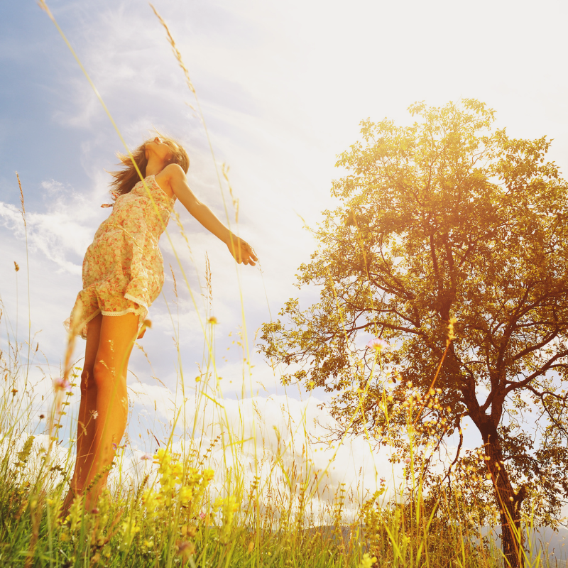A woman enjoying the warmth of sunlight in a field, symbolizing the benefits of Vitamin D and the positive effects of sunlight on mood and health
